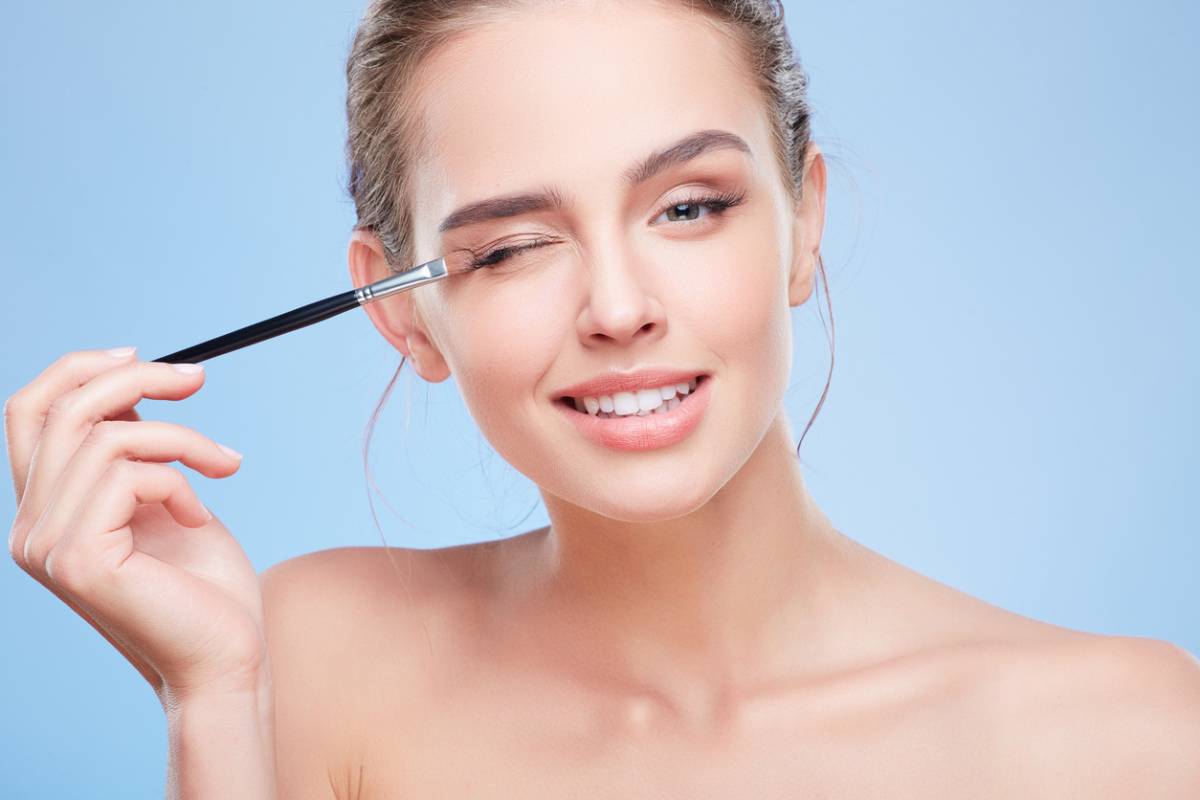 Young beautiful woman holding a brush next to her eyelids.