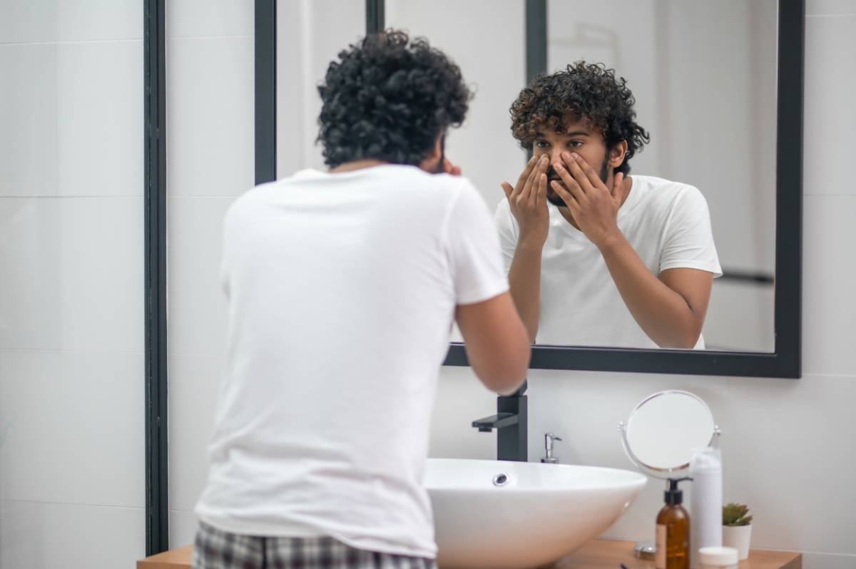 Man standing in the bathroom and staring at his skin.